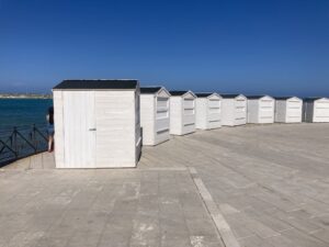 Fila di casette in legno bianco a noleggio posizionate sul lungomare per un mercatino estivo.