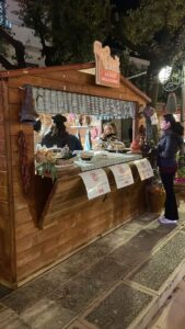 Casetta in legno da mercatino modello 3x2 metri allestita all'aperto di notte come stand gastronomico con clienti davanti al bancone espositivo.
