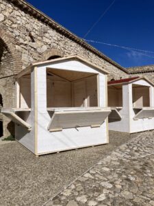 Chioschi espositivi in legno bianco a noleggio installati in un borgo antico in pietra.