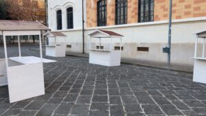 Casette in legno bianco per mercatini e fiere posizionate in una piazza per eventi.
