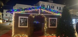 Grande casetta in legno da mercatino di Natale decorata con ghirlande luminose e luci LED colorate sul tetto di notte.