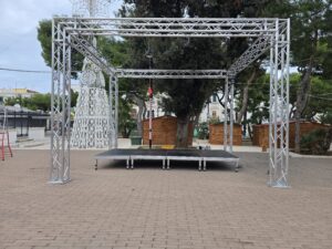 Struttura a portale in tralicci di alluminio americana con pedana e palco modulare installata in una piazza all'aperto per eventi e spettacoli.